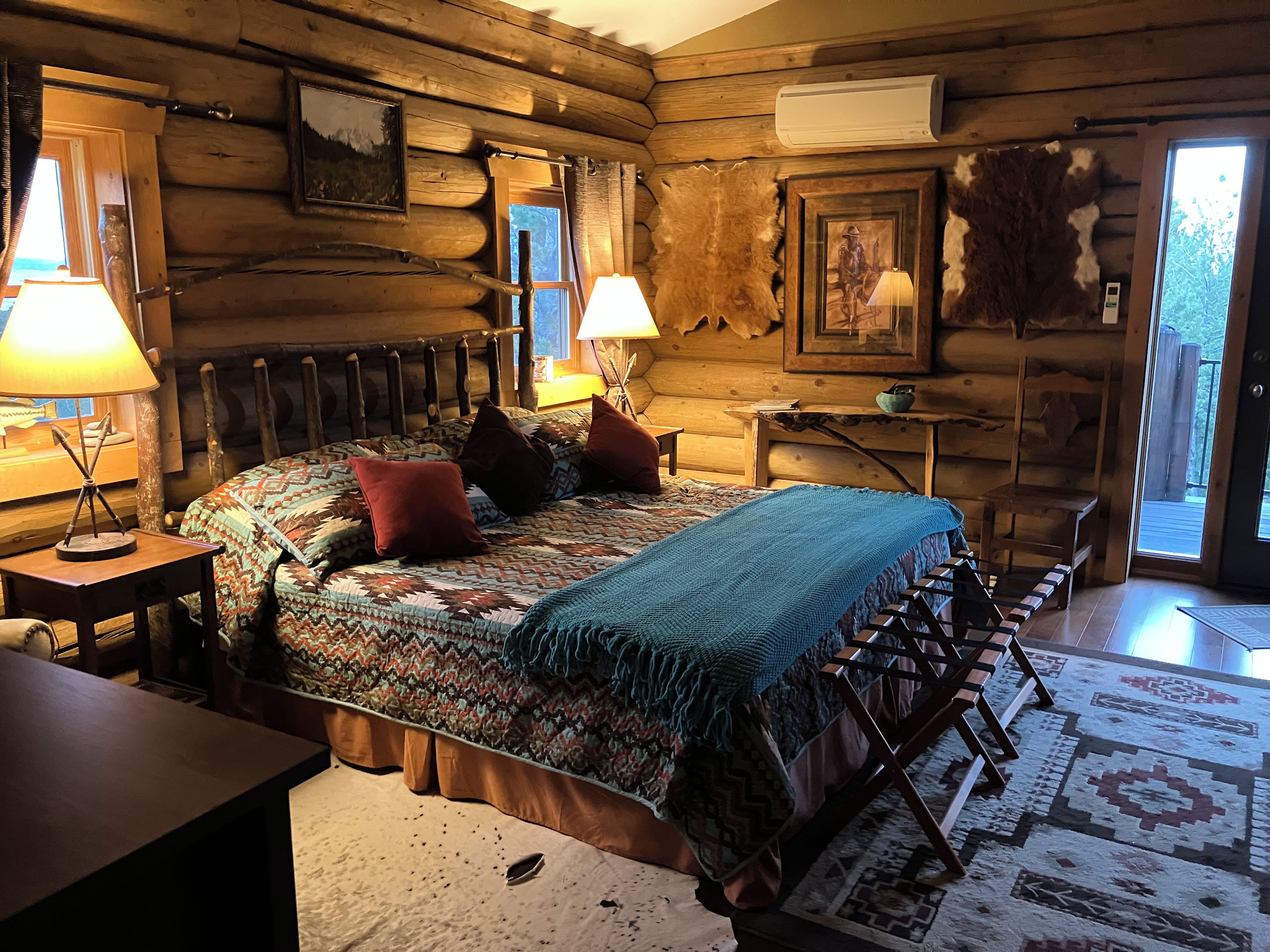 A log cabin bedroom with a bed, two lamps, a desk, and a window.