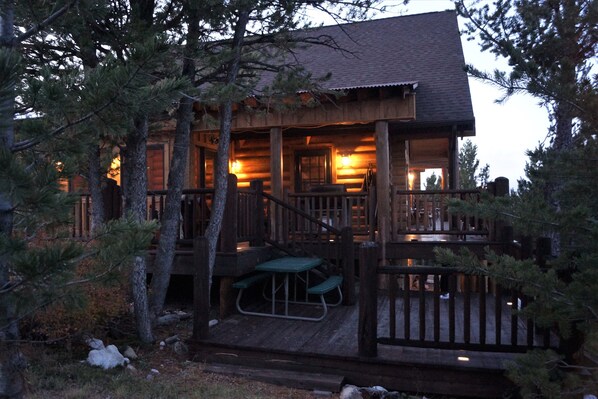 A wooden cabin with a porch, picnic table, and a covered deck area.