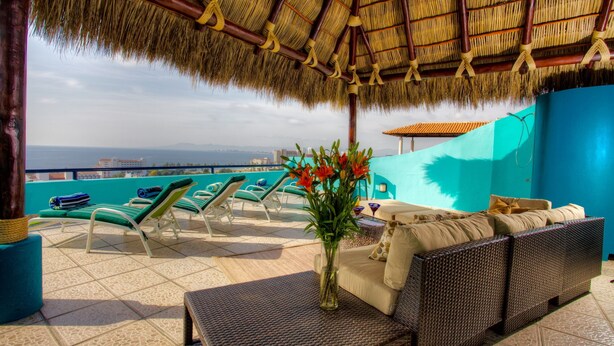 A rooftop lounge with a thatched roof, lounge chairs, a sofa, and a vase of flowers.