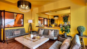 A living room with a sofa set, a coffee table, a floor lamp, and a large mirror reflecting the kitchen area.