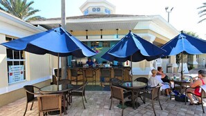 An outdoor seating area with tables and chairs, covered by blue umbrellas, and a bar in the background. -  3 miles to Disney, Private 4bed/3bath w/ private pool, game room and club house (Kissimmee)