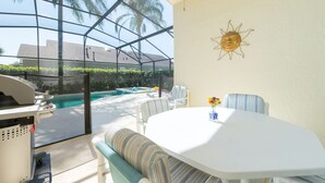 Et solrum med glasvægge, en swimmingpool, udendørs møbler og grill.