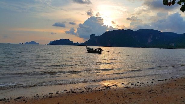 Ein Boot auf ruhigem Wasser mit Sonnenuntergang im Hintergrund und Bergen in der Ferne.