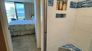 Een badkamer met douche, betegelde wanden en een klein plankje met toiletartikelen.