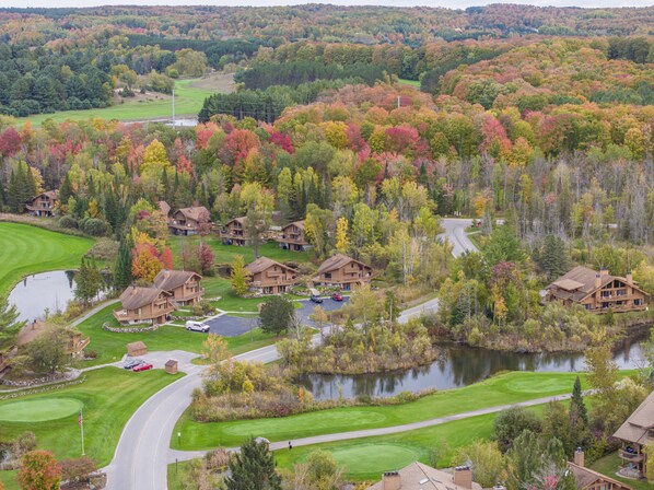 A golf course with a pond, surrounded by autumn-colored trees and multiple wooden cabins.