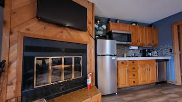 A modern kitchen with wooden cabinets, a stainless steel refrigerator, a microwave, and a flat-screen TV mounted on a wooden wall.