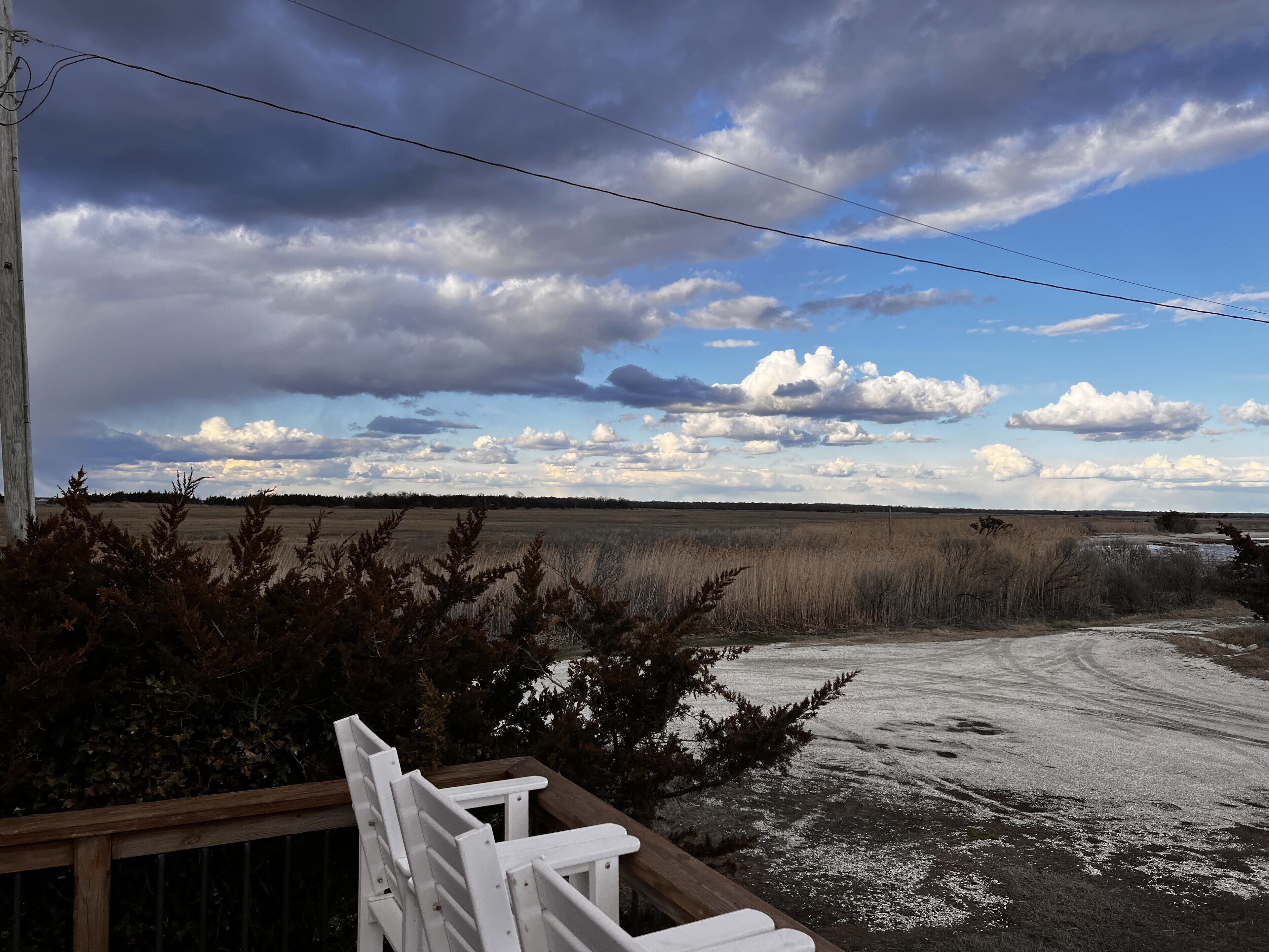 A view from a balcony overlooking a field with a wooden deck and a dirt path.