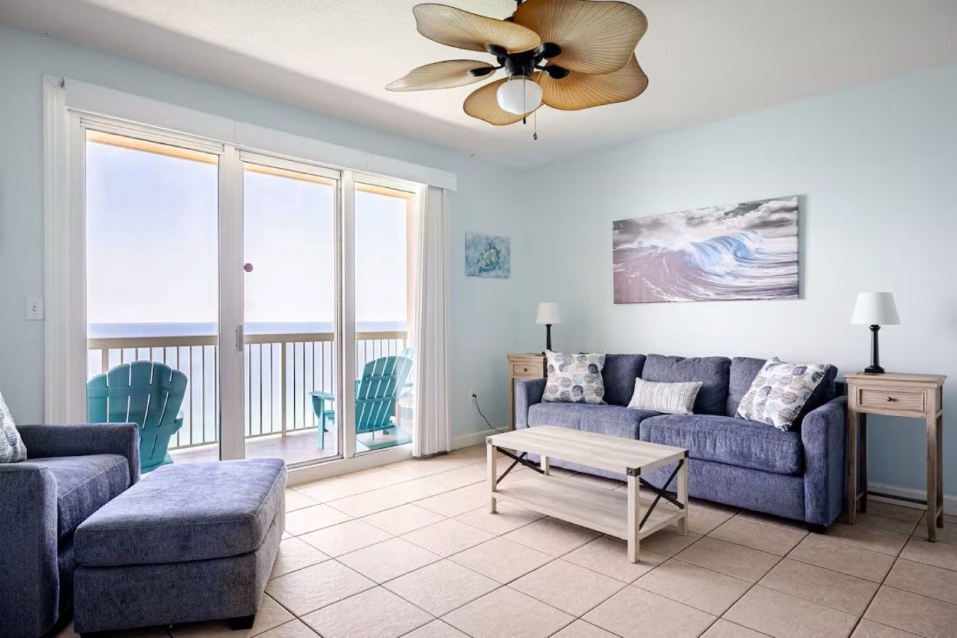 A living room with a sofa, a coffee table, a ceiling fan, and a view of the ocean through large sliding doors.