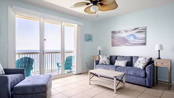 A living room with a sofa, a coffee table, a ceiling fan, and a view of the ocean through large sliding doors.