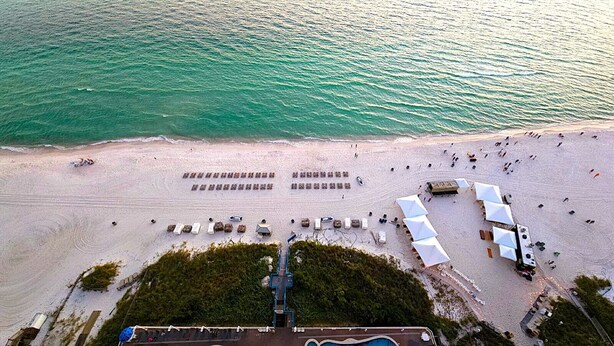 An aerial view of a beach with rows of tents and beach chairs, a pathway leading to a building, and a clear view of the ocean. - 19th floor with  beach view free beach service and 10% weekly discount (Panama City Beach)