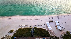 An aerial view of a beach with rows of tents and beach chairs, a pathway leading to a building, and a clear view of the ocean. - 19th floor with  beach view free beach service and 10% weekly discount (Panama City Beach)