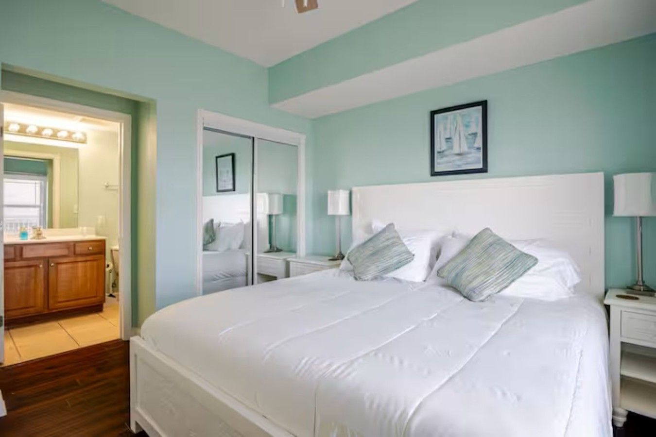 A bedroom with a large bed, a nightstand, a bedside table, and a mirror.
