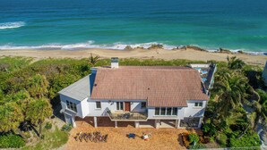 Une propriété située en bord de mer, avec une grande maison dotée d’un toit en tuiles, d’un balcon et d’une vue sur l’océan.