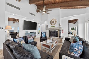 A spacious living room with a fireplace, leather sofas, a flat-screen TV, and a ceiling fan.
