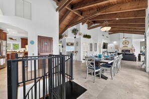 Une cuisine spacieuse avec des poutres en bois, un coin repas doté d’une longue table et un escalier avec une rampe noire.