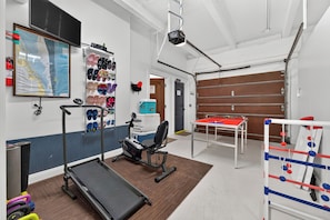 Ein Fitnessraum mit Trainingsgeräten, einem Tischtennis-Tisch und einem Boxring.
