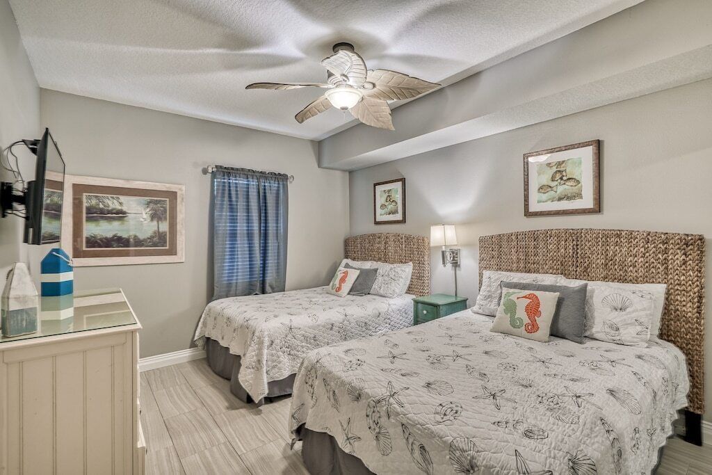 Ein Schlafzimmer mit zwei Betten, einem Deckenventilator und gerahmten Kunstwerken an den Wänden.