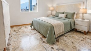 Quarto com cama, duas mesas de cabeceira, janela com vista para a cidade e ar condicionado.