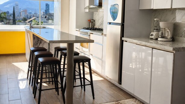 Uma cozinha moderna com uma ilha grande, banquetas, geladeira e máquina de café.