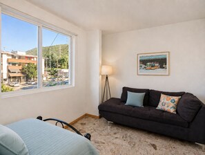 A room with a bed, a dark sofa with patterned cushions, a standing lamp, and a framed picture on the wall.