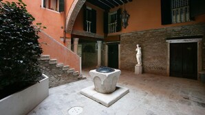 Ein Innenhof mit einem Steinfountain, einer Statue und einer Treppe, die zu einer oberen Ebene führt.