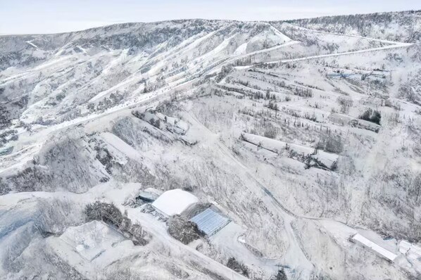 A snow-covered mountainous area with several buildings and structures, including a large white building with a flat roof and a smaller structure with a sloped roof.