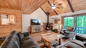 A cozy cabin interior with a fireplace, wooden ceiling, and a large window overlooking greenery. - Camelback,Aquatopia/Camelbeach Waterparks,Pool,Tennis,Jacuzzi,Paintball,Zip-line (Tannersville)