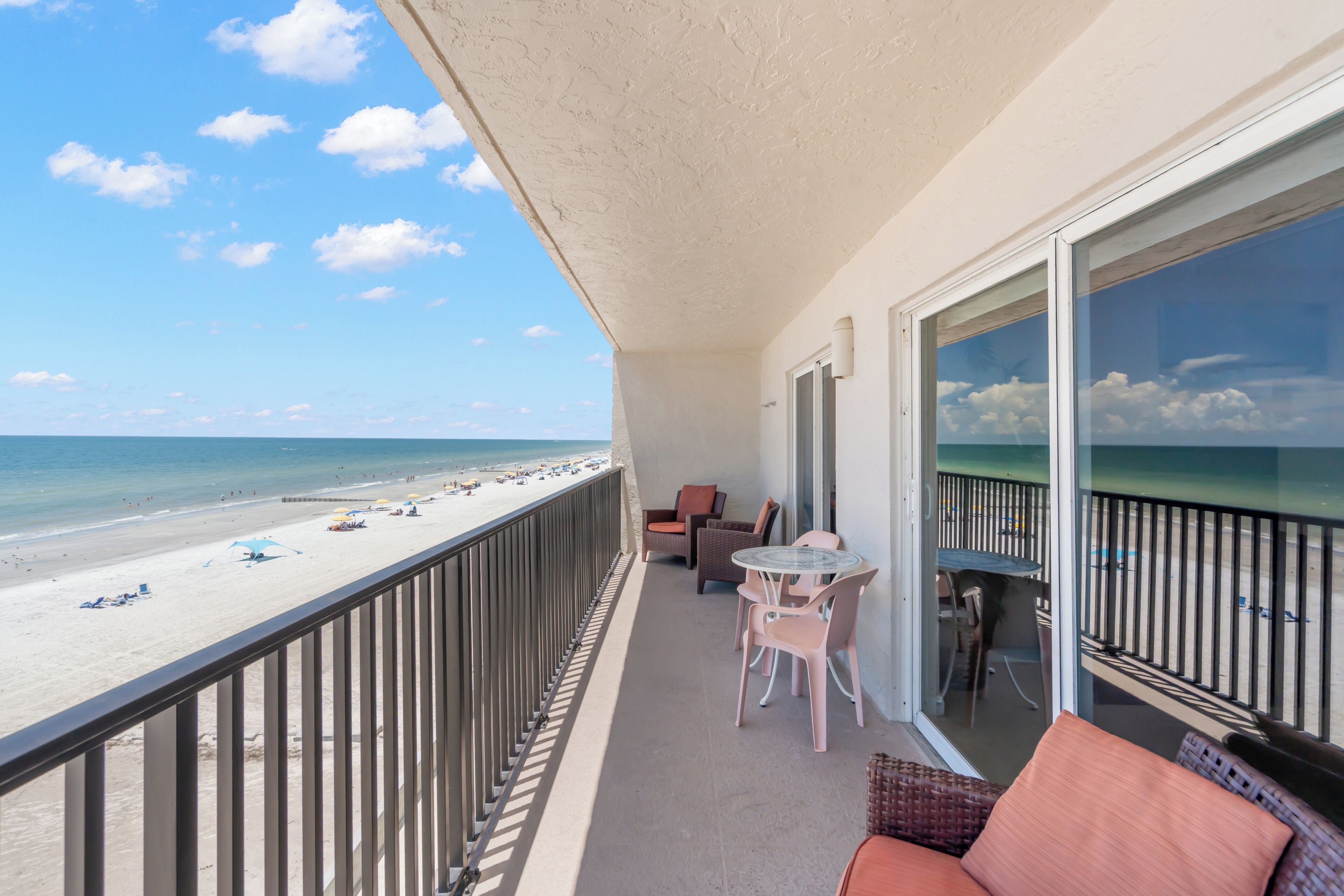 Ein Balkon mit Blick auf den Strand, einem Tisch mit Stühlen und einer Korbsitzgruppe.