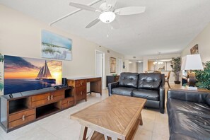 Ein Wohnzimmer mit Fernseher, einer Couch, einem Couchtisch und einem Deckenventilator.