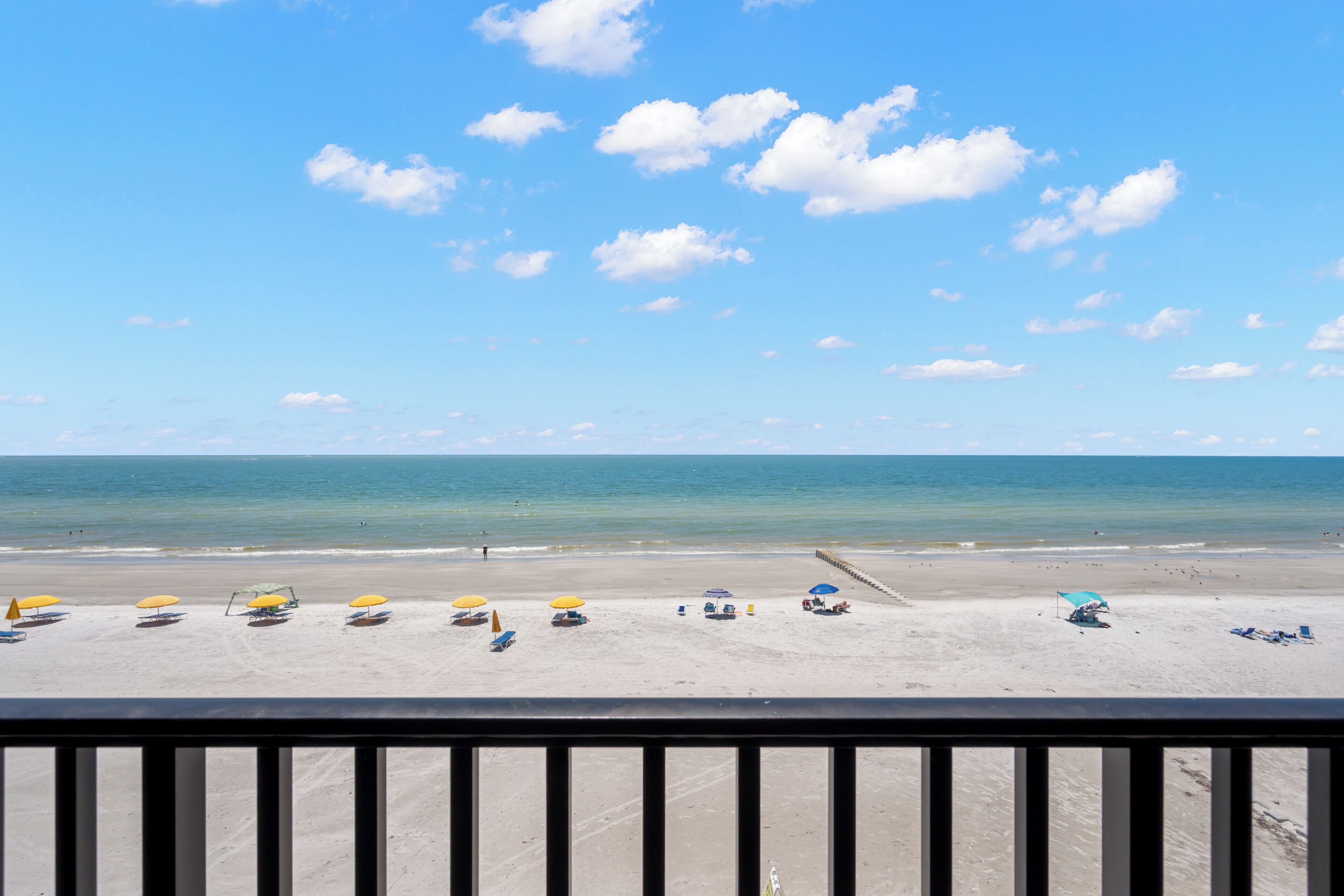 A beach with umbrellas and beach chairs, a clear sky, and the ocean.
