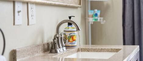A bathroom with a sink, faucet, and a soap dispenser on the countertop.