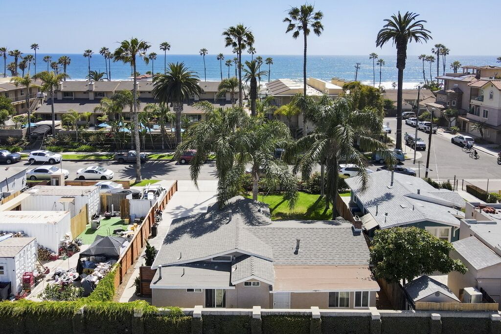 A coastal residential area with multiple houses, palm trees, and a view of the ocean.