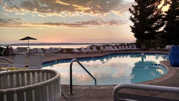 Ein Pool mit Liegestühlen und Blick auf das Meer bei Sonnenuntergang.