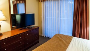 Ein Hotelzimmer mit einem Bett, einem Fernseher auf einer Holzkommode, einem Spiegel und einem Fenster mit Vorhängen.