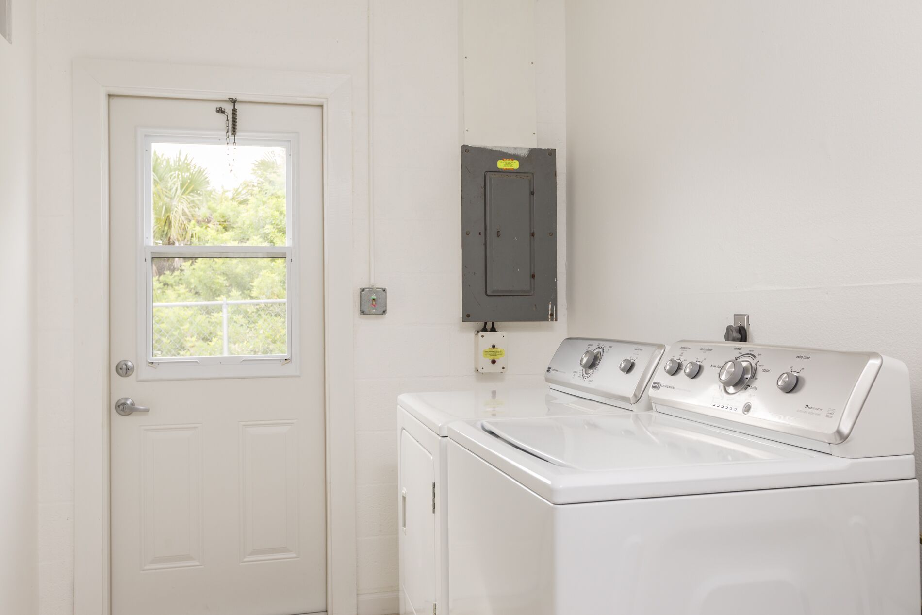 Une buanderie avec une porte blanche, une fenêtre et un tableau électrique fixé au mur.