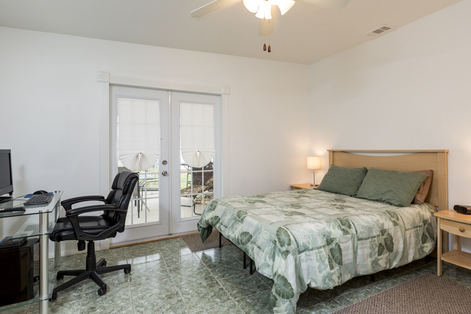 Une chambre à coucher avec un lit, un bureau avec un ordinateur, une chaise et une vue sur l’extérieur, accessible par une porte coulissante.