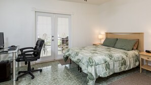 Une chambre à coucher avec un lit, un bureau avec un ordinateur, une chaise et une vue sur l’extérieur, accessible par une porte coulissante.