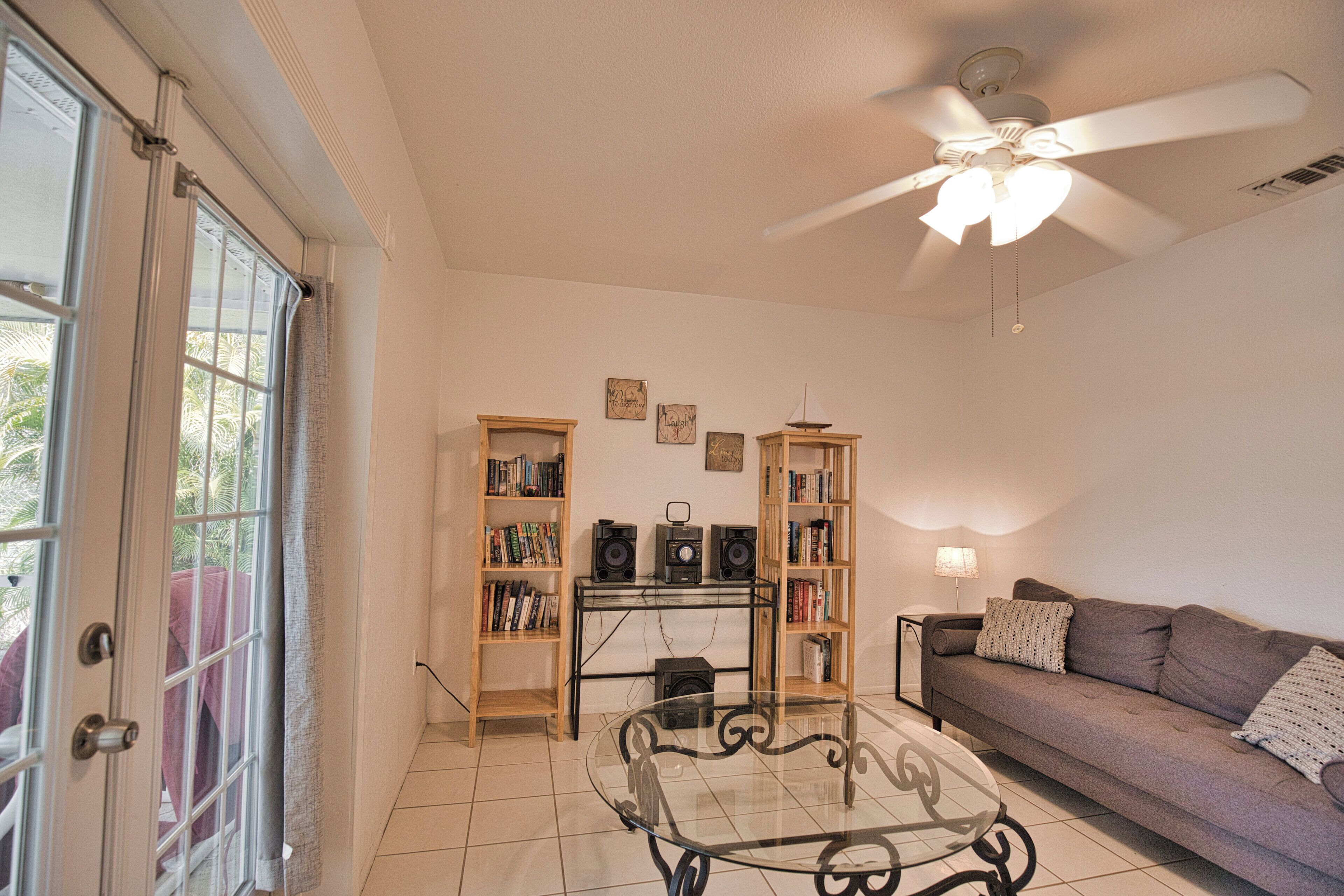 A living room with a glass coffee table, a sofa, two bookshelves, a ceiling fan, and a door with glass panels.