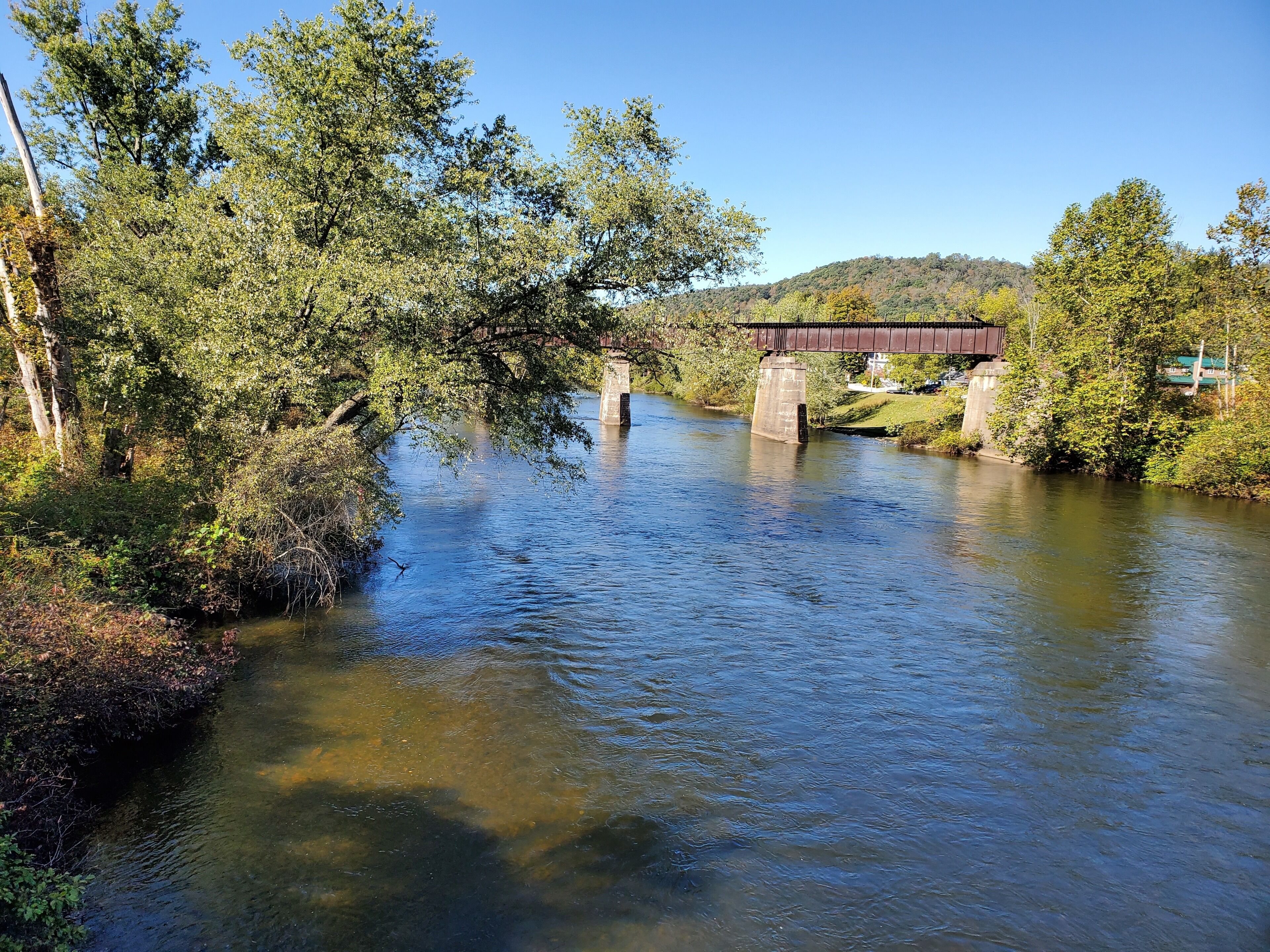 Ein Fluss mit einer Brücke, umgeben von Bäumen und Grün.