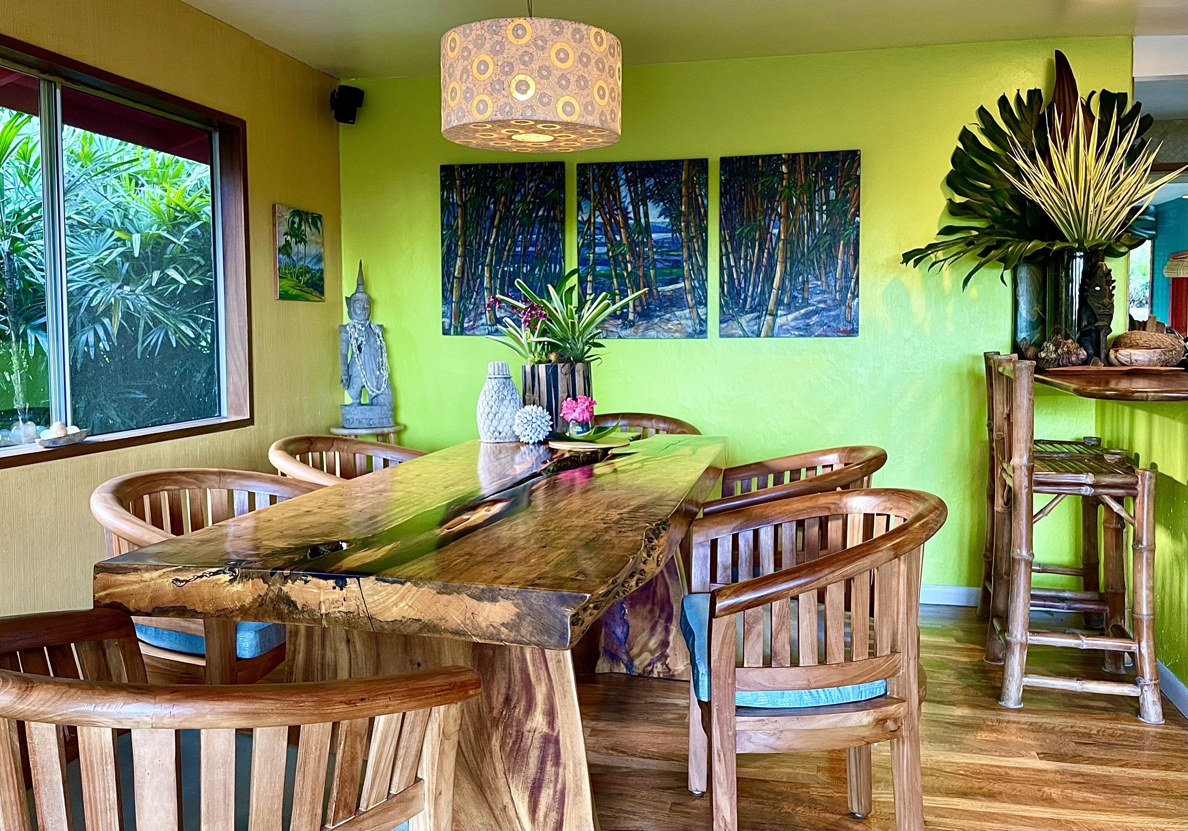 A dining area with a wooden table and chairs, surrounded by green walls and tropical artwork.