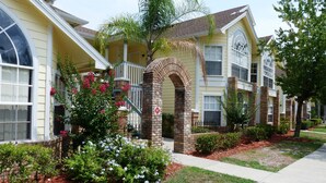 A residential building with a brick archway entrance, a covered porch, and a well-maintained garden with flowering plants. - Welcome To Potter's Castle! Near Disney, Slps 8, Harry Potter Decor, Pool, WOW! (Kissimmee)
