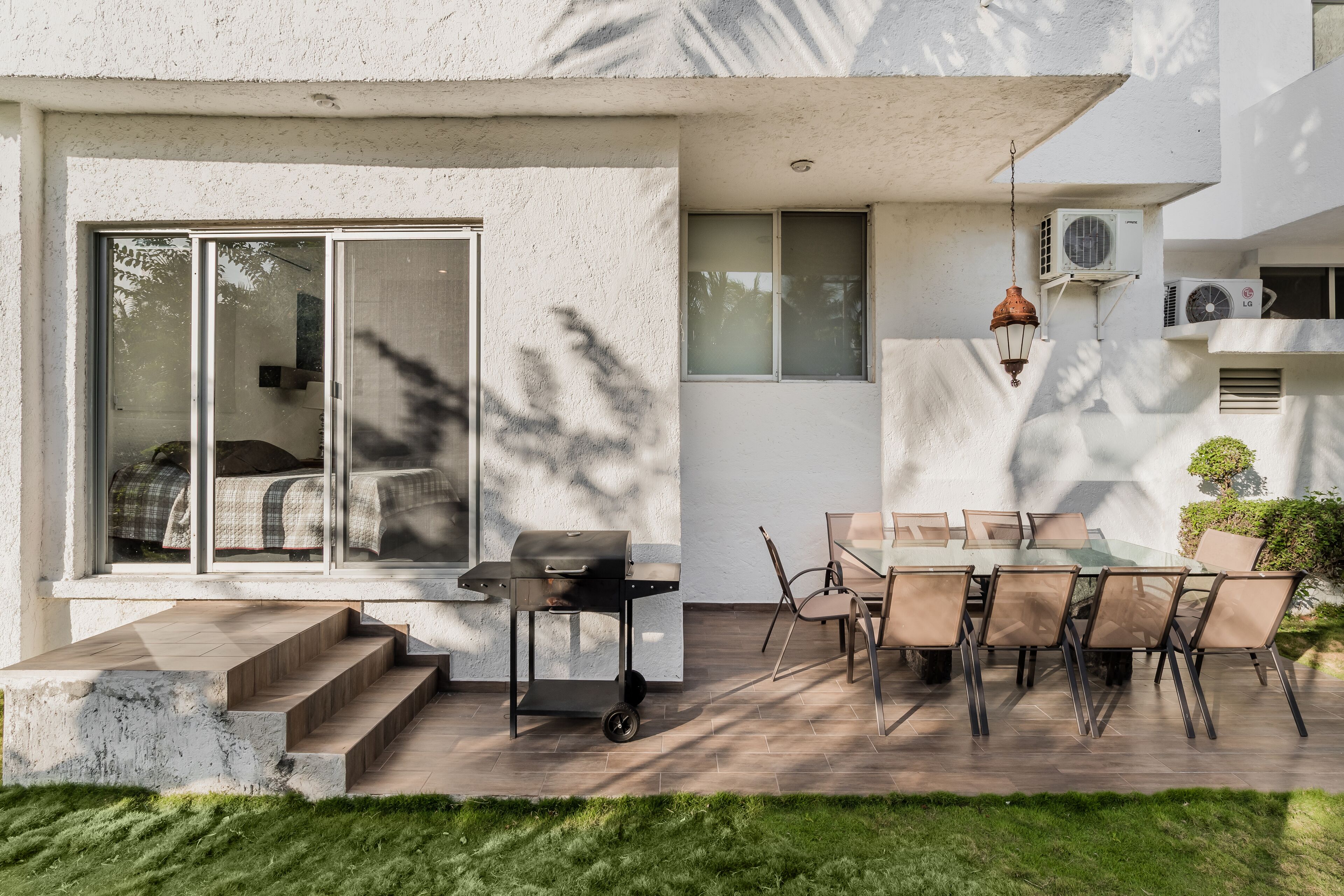 A modern outdoor patio with a dining table and chairs, a grill, and a sliding glass door leading to a bedroom.