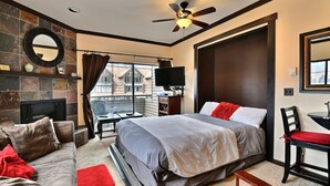 A modern hotel room with a large bed, a flat-screen TV, a fireplace, a balcony with a view, and a ceiling fan. - A+ ski-in/out REMODEL NOW 2026 @ PC pool/gym/hot tub/washer/wifi/fireplace (Park City)