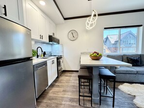 A modern kitchen with stainless steel appliances, a white countertop, and a dining area with bar stools.