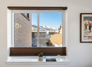 A window with a view of a mountain, a brick wall, and a poster on the wall.