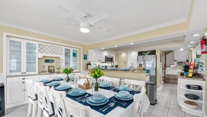 A modern kitchen with white cabinets, a dining area with blue table settings, and a ceiling fan. - As Good as it Gets: 8BR/6BA, heated pool, hot tub, private dock, ocean-to-river (Stuart)