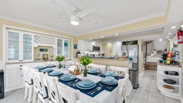 A spacious dining area with a high ceiling and a ceiling fan, a kitchen with modern appliances, and a view of the living area.