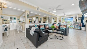 A spacious living area with a black leather sofa, a coffee table, and a kitchen area in the background. - As Good as it Gets: 8BR/6BA, heated pool, hot tub, private dock, ocean-to-river (Stuart)