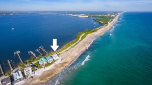An aerial view of a coastal area with a beach, a pier, and a building with a green roof. - As Good as it Gets: 8BR/6BA, heated pool, hot tub, private dock, ocean-to-river (Stuart)
