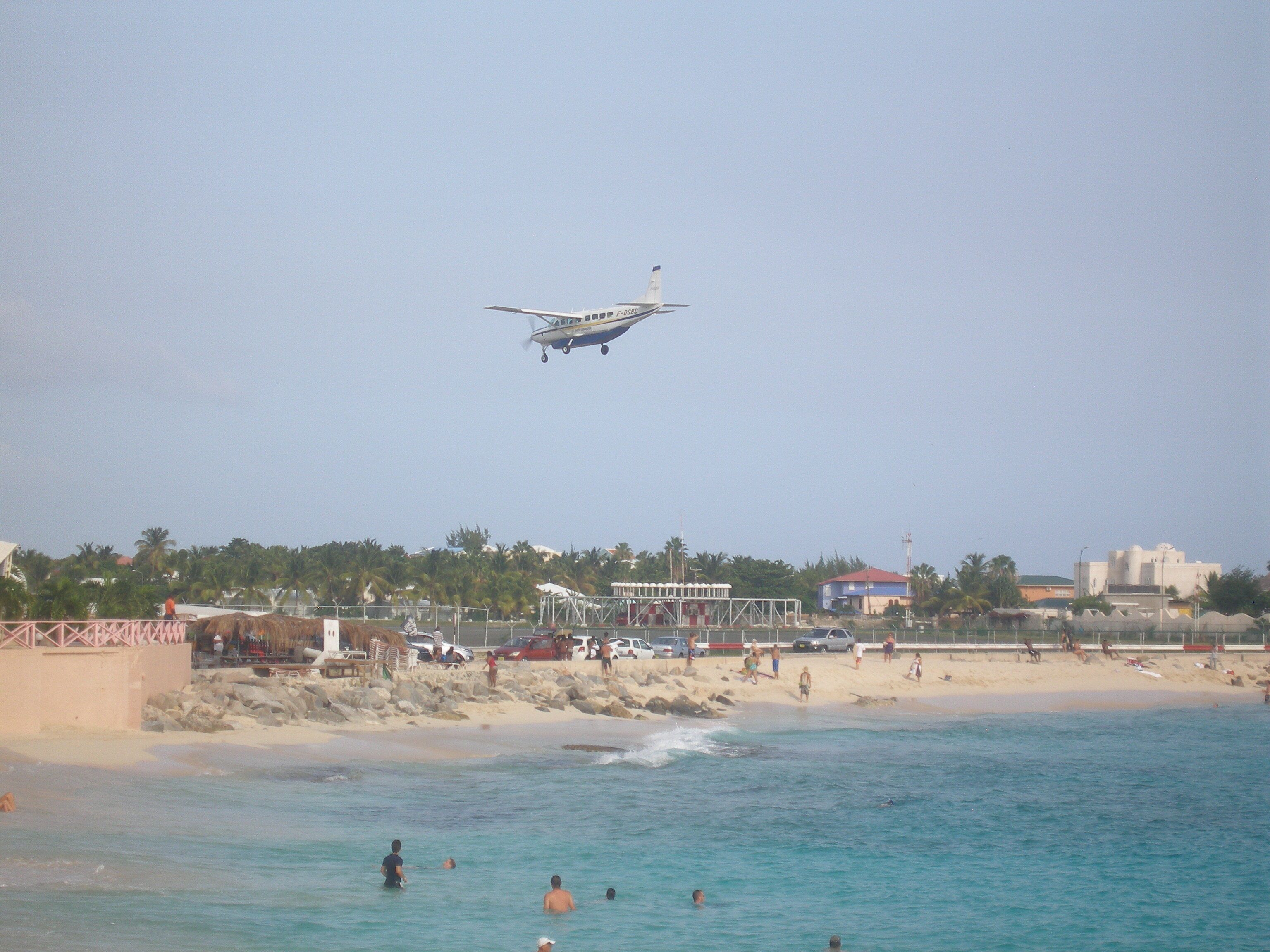 Una spiaggia con persone che nuotano e un piccolo aereo che vola sopra.